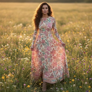 May include: A long, flowing dress with a floral pattern in shades of pink, red, and green. The dress has long sleeves and a round neckline. The woman is standing in a field of wildflowers, with the sun setting in the background.