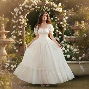 May include: A white, floor-length dress with a square neckline and puff sleeves. The dress is worn in a garden setting with white roses and a stone fountain. The dress has a ruffled hemline and a fitted bodice.