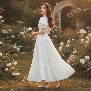 May include: A long, white dress with short, puffed sleeves and a flowing skirt. The dress features a ruffled hem and is worn in a garden setting with white roses. The dress is a classic, romantic style.