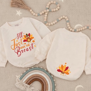 May include: Two cream-colored long-sleeve sweatshirts. The left sweatshirt features a graphic of a turkey wearing a hat with the text "I'll Just Have The Breast" in orange and red. The right sweatshirt features a small graphic of a turkey on the back.
