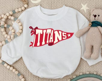 May include: White baby bodysuit with long sleeves. The bodysuit features a red pennant design with the word "TITANS" in white block letters. A red star is on the right side of the pennant. The bodysuit is surrounded by decorative items.