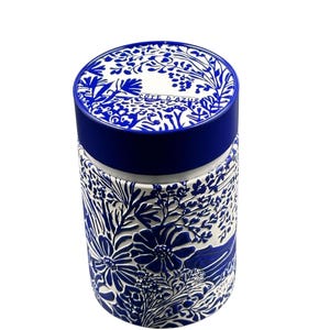 Könnte beinhalten: Ein zylindrischer Behälter mit blauem und weißem Blumendesign. Der Deckel trägt den weißen Schriftzug "COTE D'AZUR". Der Körper des Behälters ist mit einem detaillierten Reliefmuster aus Blumen und Blättern verziert.