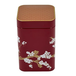 Könnte beinhalten: Eine rechteckige, weinrote Dose mit einem goldfarbenen, gemusterten Deckel. Die Dose ist mit einem goldenen Astdesign und weißen Blüten verziert. Die Dose wird wahrscheinlich zur Aufbewahrung verwendet.
