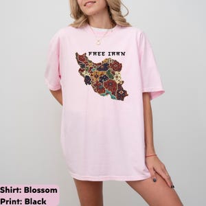 以下が含まれることがあります： 「FREE IRAN」の文字と、イランのカラフルな地図がプリントされたライトピンクのTシャツ。 地図のデザインは、赤、青、黄色、茶色の複雑なパターンが特徴です。 このTシャツはカジュアルなスタイルです。