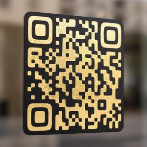 May include: A black QR code with gold-colored details. The code is rectangular with rounded corners and is likely used for digital information access. The gold color provides a contrasting visual element against the black background.