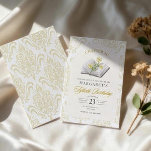 May include: An invitation for Margaret's Fiftieth Birthday, featuring a floral design and the text "Chapter 50." The invitation is cream-colored with gold accents and a matching patterned card. Dried flowers are arranged nearby.