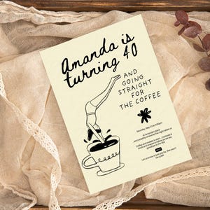 Könnte beinhalten: Eine cremefarbene Einladungskarte mit schwarzem Text, der lautet: "Amanda wird 40" und "Und geht direkt zum Kaffee". Die Karte zeigt eine skurrile Illustration einer Person, die in eine Kaffeetasse springt. Die Einladung liegt auf einem Holztablett mit Stoff und Spitze.