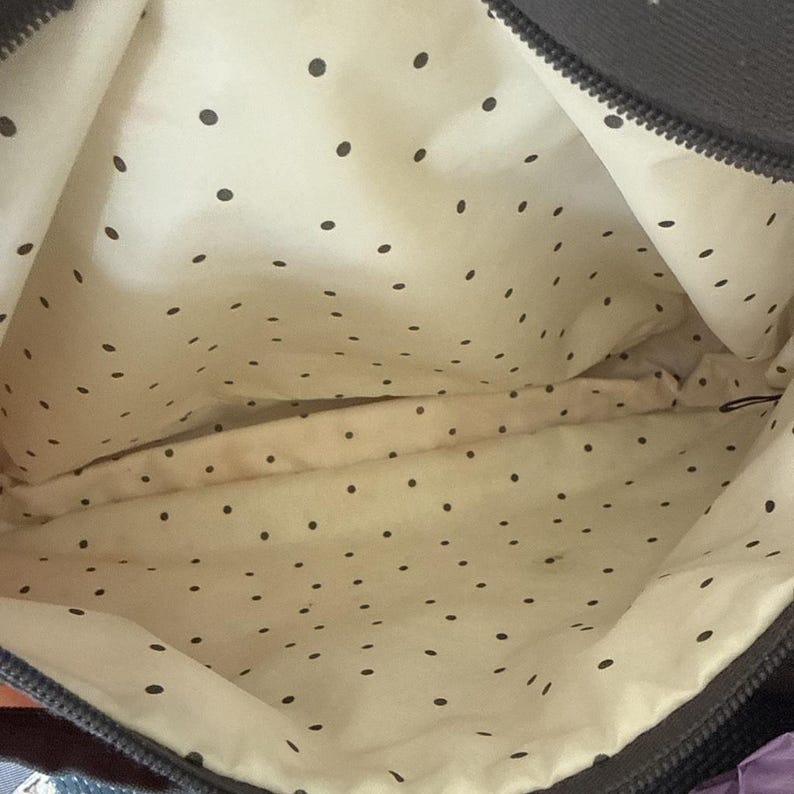 May include: Interior view of a dark gray tote bag. The inside lining is cream-colored with a pattern of small black polka dots. The bag's zipper is visible along the top edge.