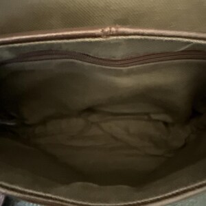 May include: Open view of a brown leather bag interior. The bag has a zippered pocket at the top and a light brown fabric lining. The bag's interior is empty.