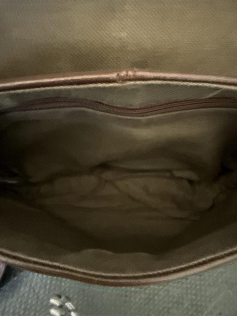 May include: Open view of a brown leather bag interior. The bag has a zippered pocket at the top and a light brown fabric lining. The bag's interior is empty.