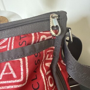 May include: Red and white patterned crossbody bag with gray trim and a silver zipper pull. The bag features the word "CLASS" in large white letters. The zipper pull has a heart-shaped design.