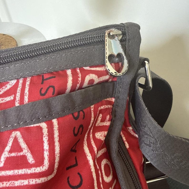 May include: Red and white patterned crossbody bag with gray trim and a silver zipper pull. The bag features the word "CLASS" in large white letters. The zipper pull has a heart-shaped design.
