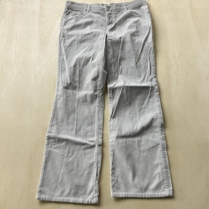 Könnte beinhalten: Eine hellgraue Cordhose mit ausgestelltem Bein. Die Hose hat einen Knopf- und Reißverschluss, Gürtelschlaufen und Taschen. Der Cordstoff hat ein weiches, strukturiertes Aussehen.