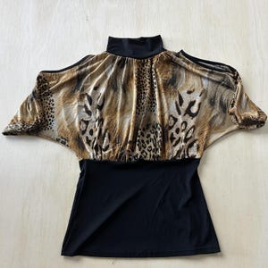 May include: A black and leopard print top with a high neck and open shoulders. The top features a black bottom and a leopard print pattern on the upper portion, with a mix of brown, tan, and black spots.