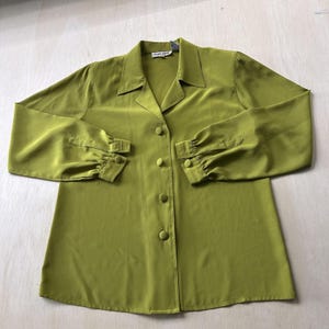 May include: A long-sleeved button-down shirt in a solid chartreuse green color. The shirt features a classic collar, a front placket with four matching fabric-covered buttons, and long sleeves that gather at the cuffs with a single button closure.