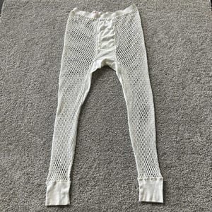 May include: Off-white long underwear pants featuring a wide-gauge fishnet mesh construction throughout the legs. The garment includes a solid fabric crotch panel, a thick elasticized waistband, and ribbed cuffs at the bottom of each leg opening.