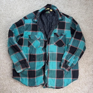 May include: A long-sleeve button-up shirt featuring a teal and black plaid pattern with thin red accent lines. The shirt has a black quilted interior lining, a standard collar, two chest pockets with button flaps, and buttoned cuffs.