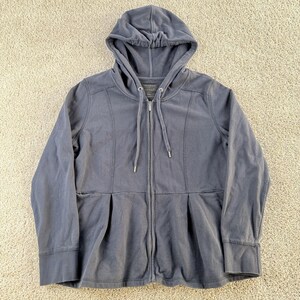 Könnte beinhalten: Ein schieferblauer Kapuzenpullover mit Reißverschluss und Kordelzug. Die Jacke hat ein plissiertes Design an der Taille, zwei Vordertaschen und gerippte Bündchen. Der Markenname "Weatherwick House" ist sichtbar.