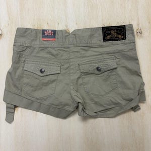 May include: Khaki shorts with two back pockets and button fastenings. The shorts feature a rolled hem and belt loops. The brand name "TOXIC" is visible on a tag at the back. Made from a lightweight fabric, these shorts are ideal for warmer weather.