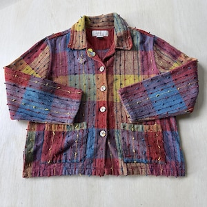 May include: A long-sleeve button-up jacket featuring a multi-colored plaid pattern in red, blue, and yellow. The fabric has a textured surface with small raised tufts and two front pockets. A small heart-shaped pin is attached to the chest.