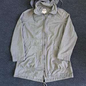 May include: A light gray hooded jacket with a full-length zipper, drawstring waist, and two front pockets. The jacket has a Mossimo Supply Co. label and is made of a lightweight material.