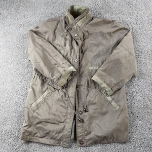 May include: A tan-colored, long coat with a high collar and button-up front. The coat features a drawstring waist, two front pockets, and olive green trim on the cuffs and collar. The coat is made of a lightweight material.