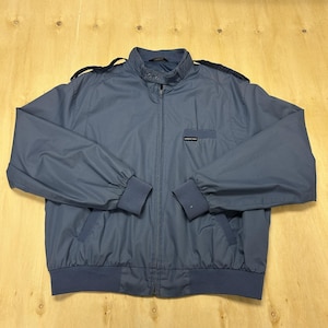 May include: A slate blue Members Only jacket featuring a stand-up collar with a snap closure, shoulder epaulets, a full-length front zipper, ribbed cuffs and hem, and a small chest pocket with a black brand label reading Members Only.