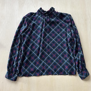 May include: A long-sleeved top with a high neckline. The top features a plaid pattern in shades of blue, green, red, and white. The fabric appears to be soft and comfortable, with a slight sheen. The cuffs and neckline are finished with a matching fabric.