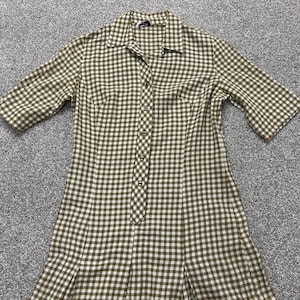 May include: A knee-length dress featuring a brown and white gingham check pattern, a pointed collar, and short sleeves. The garment has a central button-down placket with six visible buttons and vertical seams extending from the bodice to the hem.