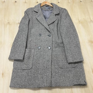 May include: A double-breasted coat in a grey and white herringbone pattern. The coat features a notched lapel, long sleeves, two front patch pockets, and four dark buttons arranged in two vertical rows on the front. It has a grey lining.
