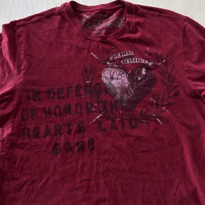 Puede incluir: Una camiseta burdeos de Express con un diseño de corazón. El diseño incluye las frases "In Defense of Honor" y "Love Knows No Despair". La camiseta tiene cuello redondo y mangas cortas.