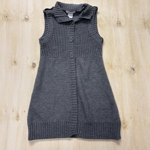 May include: A sleeveless, charcoal gray sweater vest with a collared neckline and button-down front. The upper chest area features a textured knit pattern, while the lower portion has a ribbed hem. The vest is made of a soft, knitted material.