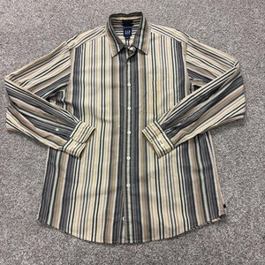 Könnte beinhalten: Ein langärmeliges Hemd mit Knopfleiste und vertikalem Streifenmuster in den Farben Beige, Dunkelgrau, Creme und Schwarz. Das Hemd hat einen klassischen Kragen, eine durchgehende Knopfleiste und geknöpfte Manschetten. Ein Gap-Markenetikett ist am Kragen sichtbar.