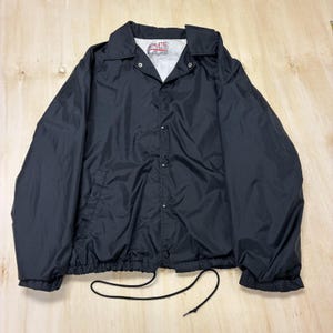 May include: Black athletic jacket with a button-up front, collar, and elastic cuffs. The jacket has a drawstring at the bottom hem and a small logo on the inside. The jacket is made of a lightweight material.