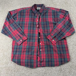 Puede incluir: Una camisa a cuadros con botones en rojo, verde y azul marino. La camisa de manga larga presenta un patrón de cuadros clásico con botones blancos y cuello. La tela es tejida.