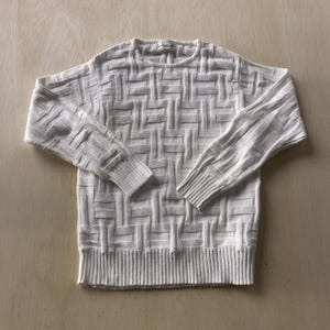 May include: Off-white sweater with a textured geometric pattern. The crew neck sweater has long sleeves with ribbed cuffs and a ribbed hem. The knitwear is made of a soft material.