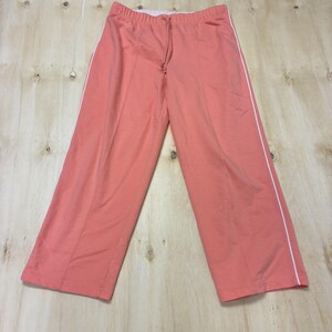 May include: Coral-colored wide-leg pants featuring a white vertical stripe running down the outer side of each leg. The pants have an elastic waistband with a matching coral drawstring, a center seam detail on the front, and a straight-leg cut.
