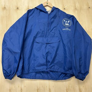 May include: A royal blue pullover windbreaker jacket with a hood, a half-zip front, and a front pouch pocket. The chest features a circular logo with the text "Celebrating 40 Years of Manufacturing Excellence" and "40th Anniversary" in white.