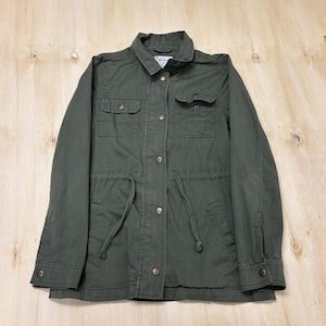 May include: An olive green utility jacket featuring a collared neckline, long sleeves with buttoned cuffs, and a front button closure. The jacket includes two chest pockets with flaps, two lower pockets, and a drawstring waist with two fabric ties.