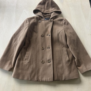 May include: A tan hooded coat with a double-breasted design. The coat features six brown buttons, two front pockets, and a tailored fit. The hood is attached, and the coat is made of a soft, warm material.