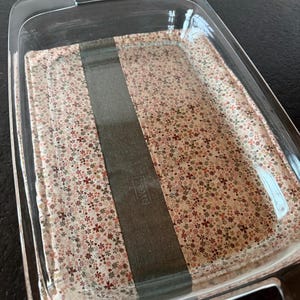 May include: A clear glass baking dish with a floral patterned insert. The insert features a cream background with small red, brown, and green flowers. A dark gray band is centered on the insert.