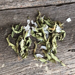 May include: Dried lemon verbena leaves and shredded coconut on a rustic wooden surface.