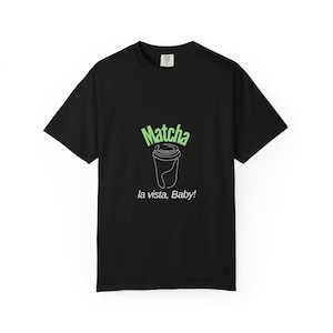 Könnte beinhalten: Schwarzes T-Shirt mit einer grünen Grafik eines Matcha-Getränks und dem Text "Matcha la vista, Baby!". Das Design zeigt eine Strichzeichnung eines To-Go-Bechers. Das Shirt hat kurze Ärmel und einen Rundhalsausschnitt.
