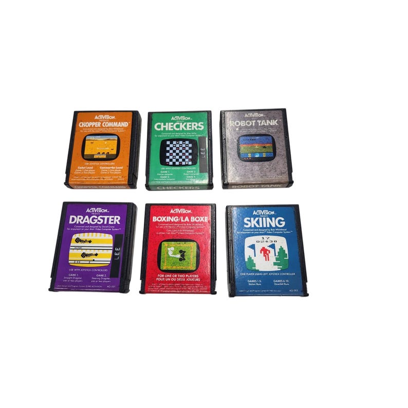 May include: A collection of six vintage Activision video game cartridges. Titles include "Chopper Command," "Checkers," "Robot Tank," "Dragster," "Boxing/La Boxe," and "Skiing." Each cartridge features colorful game graphics and text.