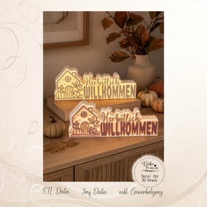 Könnte beinhalten: Zwei beleuchtete weiße Dekoschilder mit Hausumriss, Kürbis- und Blattmotiven sowie dem deutschen Schriftzug "Herbstlich WILLKOMMEN" im Scherenschnitt-Stil, platziert auf einer Holzoberfläche neben kleinen Kürbissen.
