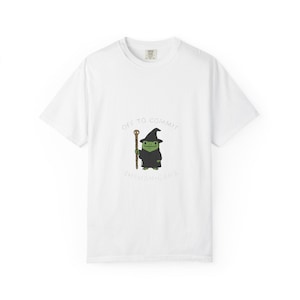 May include: White t-shirt featuring a cartoon frog in a wizard costume, holding a staff. The text "OFF TO COMMIT SHENANIGANS" is arched above and below the frog illustration. The shirt has a crew neck and short sleeves.