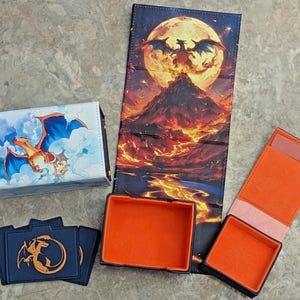 May include: A collection of card game accessories featuring a dragon theme. Includes a card box with a dragon and cloud design, a playmat with a dragon and volcano scene, and card sleeves with a dragon emblem. The interiors are orange.