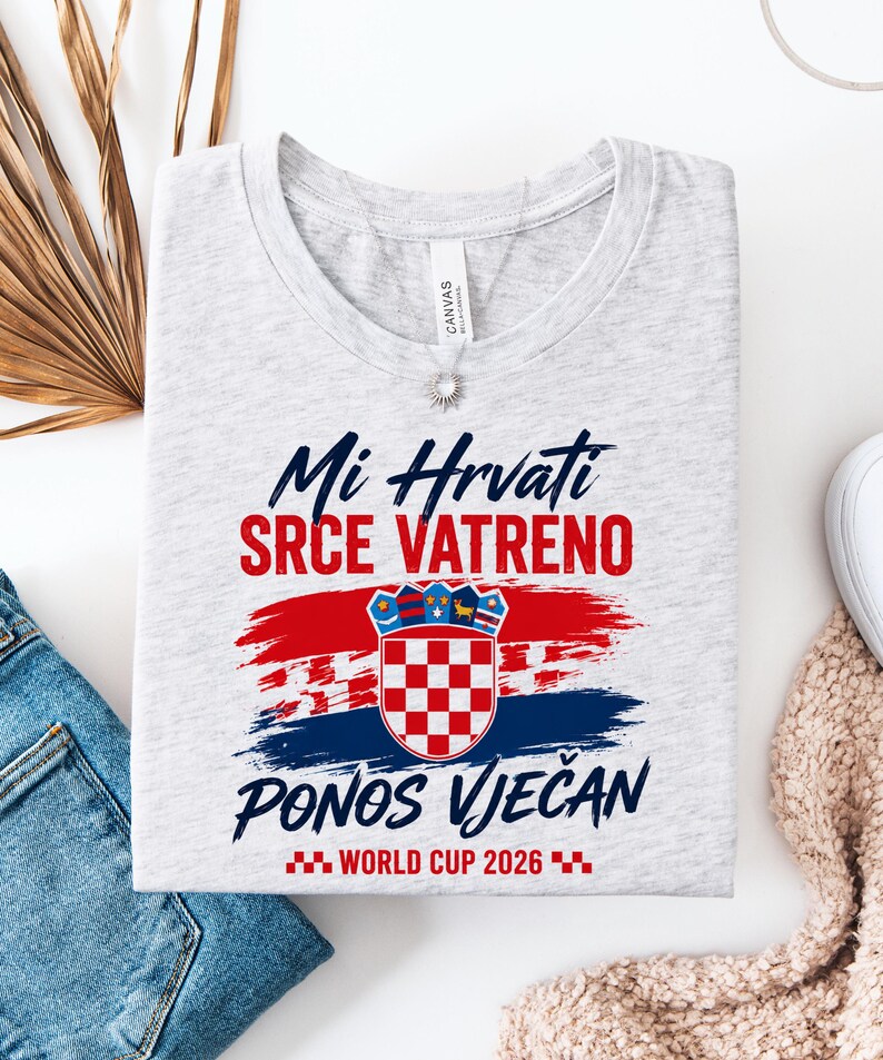 May include: A light gray t-shirt with the Croatian coat of arms and text in red and blue. The text reads "Mi Hrvati Srce Vatreno Ponos Vječan World Cup 2026". The design features red and blue brushstrokes.
