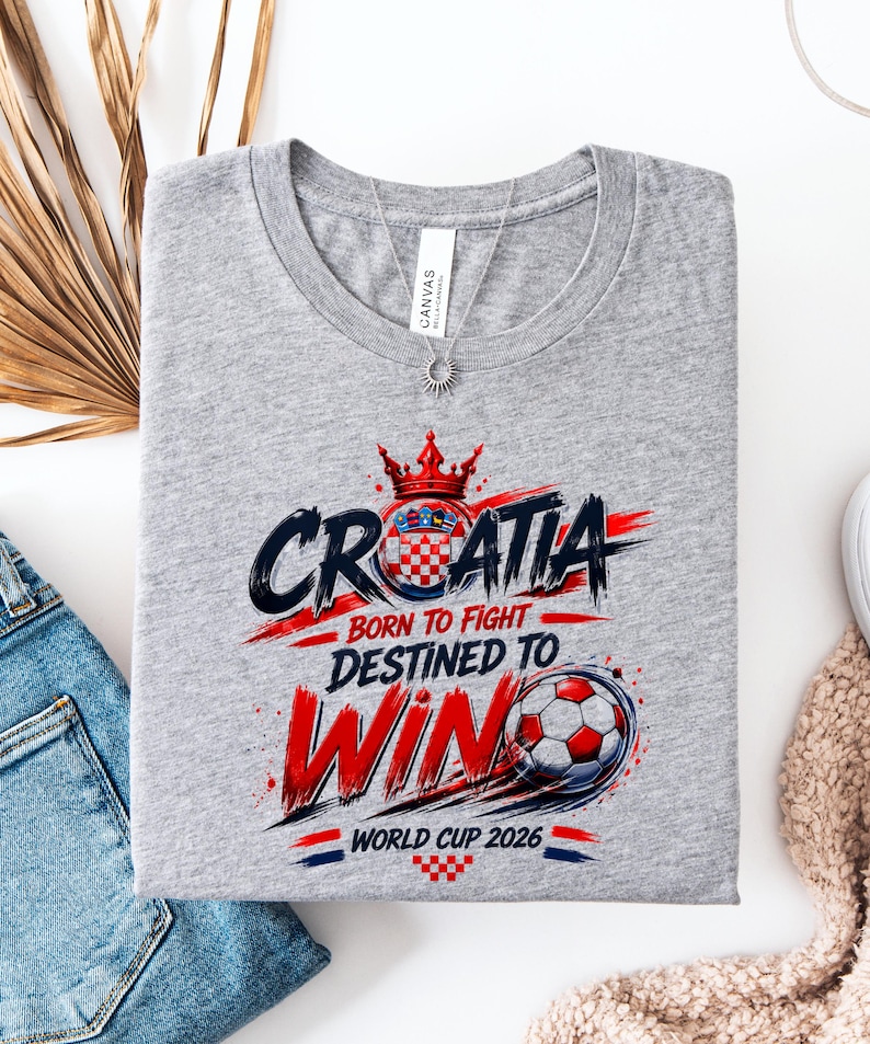May include: A gray t-shirt with a graphic design featuring the word "CROATIA" in a bold, stylized font, along with the phrases "BORN TO FIGHT" and "DESTINED TO WIN." A soccer ball and the text "WORLD CUP 2026" are also included.