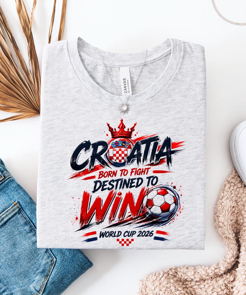 May include: A light gray t-shirt with a graphic design featuring the word "CROATIA" in black and red, a Croatian coat of arms, and the text "BORN TO FIGHT DESTINED TO WIN WORLD CUP 2026". A soccer ball is also featured.